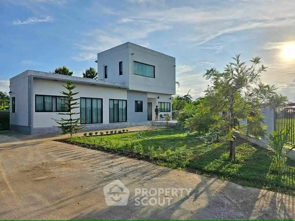 Modern two-story house with large windows and lush garden, showcasing contemporary architecture and serene surroundings.