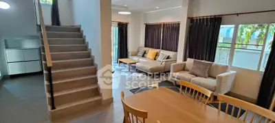 Spacious living room with modern furniture and natural light, featuring a staircase and dining area.