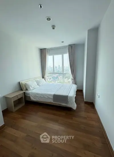 Bright bedroom with city view, wooden flooring, and modern furnishings in a high-rise apartment.