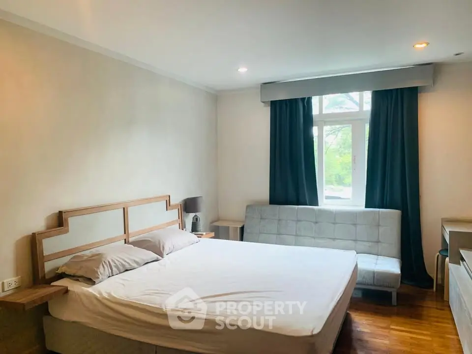 Spacious bedroom with large window and modern furnishings in a cozy apartment.