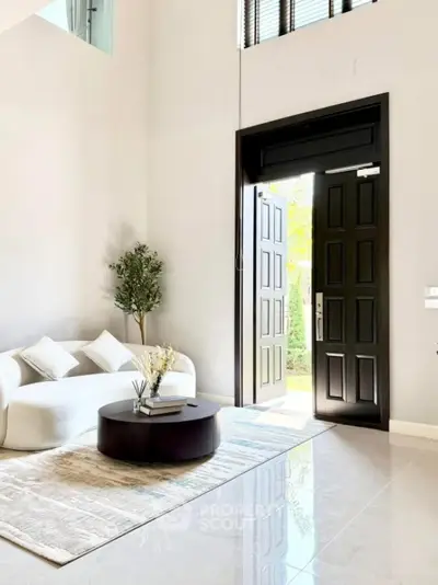 Elegant living room with high ceilings, modern furniture, and open door to garden view.
