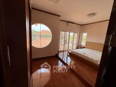 Spacious bedroom with polished wooden floors and large windows offering natural light.