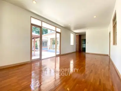 Spacious living room with wooden flooring and large windows overlooking patio