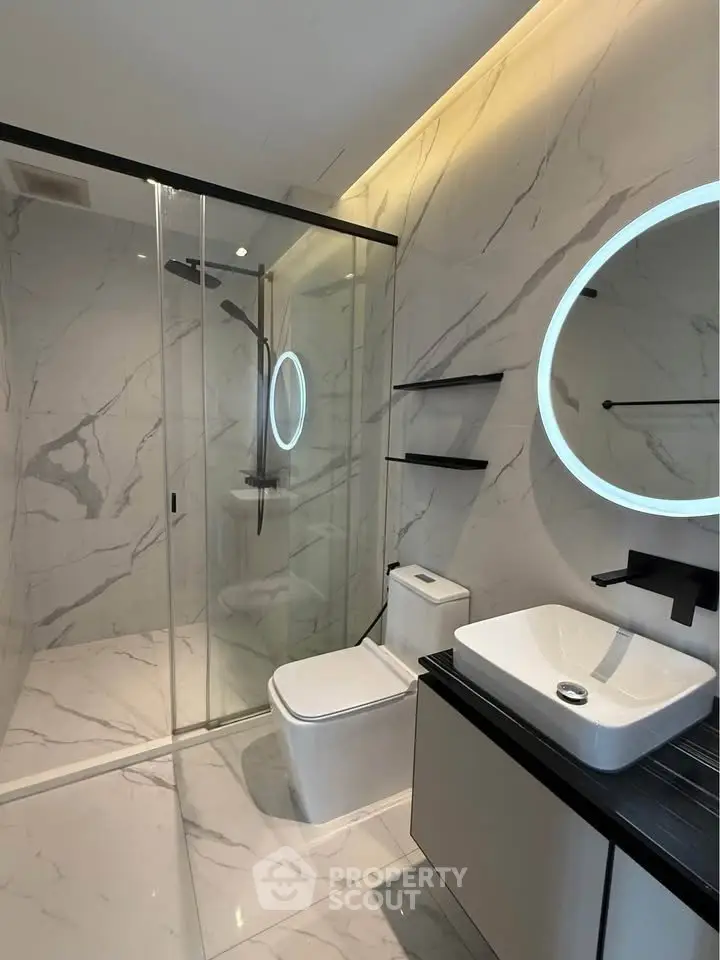 Luxurious modern bathroom with marble walls, glass shower, and illuminated mirror