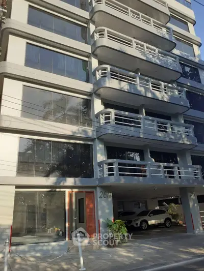 Modern multi-story building with balconies and parking area in urban setting.