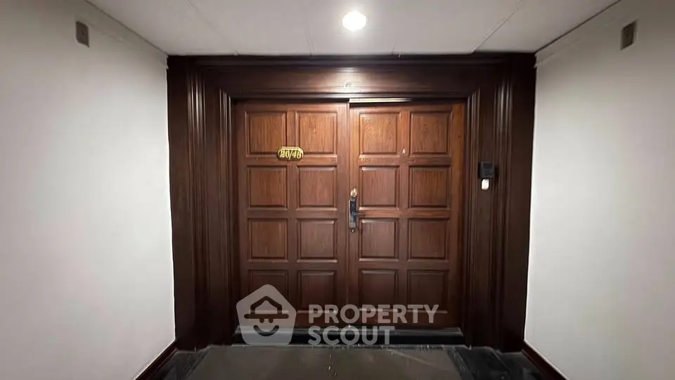 Elegant wooden entrance door with intricate panel design in a well-lit hallway.