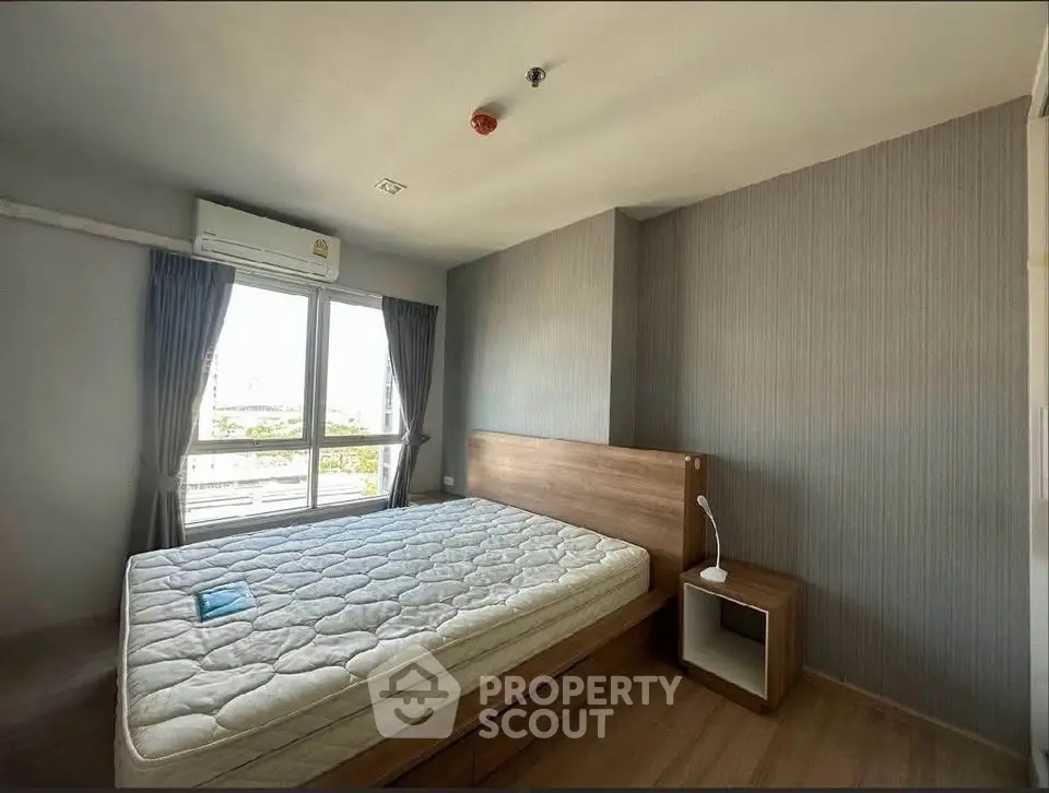 Spacious bedroom with large window and modern furnishings in a well-lit apartment.