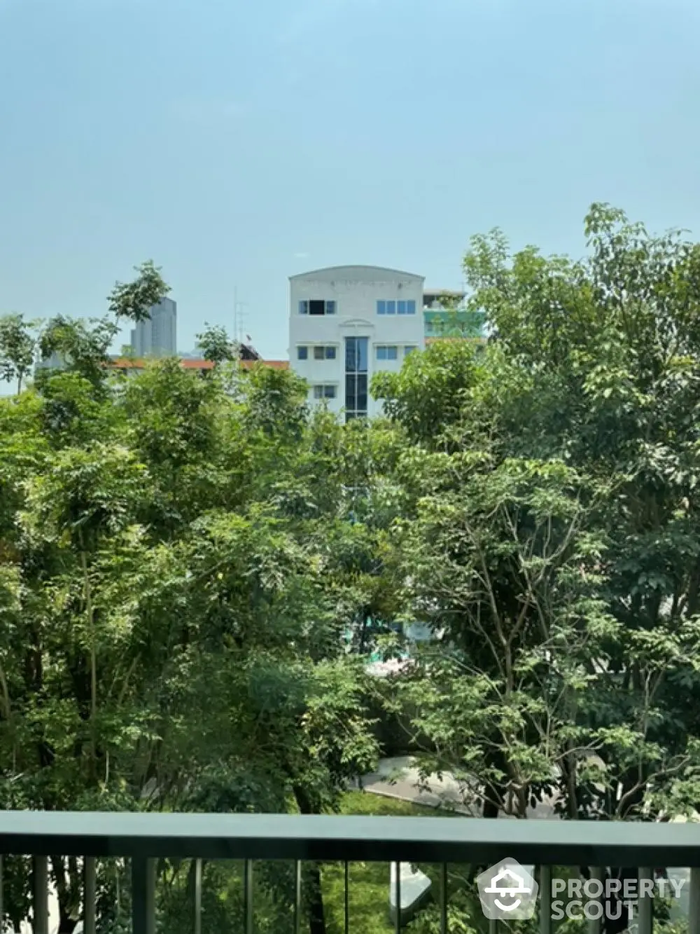 Scenic view from balcony overlooking lush greenery and distant building.