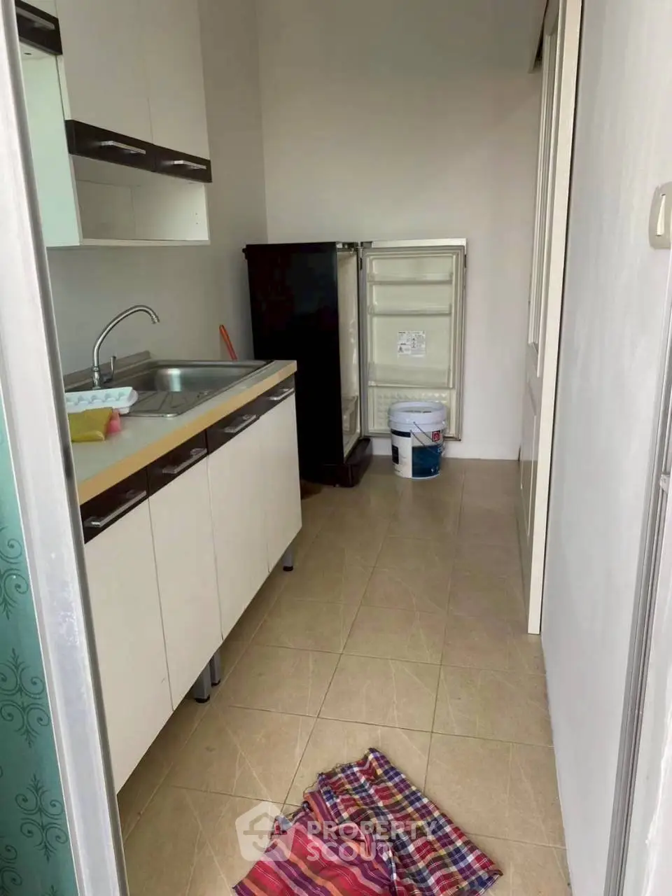 Compact kitchen with open fridge and modern cabinetry in cozy apartment.