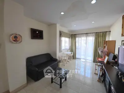 Cozy living room with natural light, black sofa, and glass coffee table in a modern apartment.