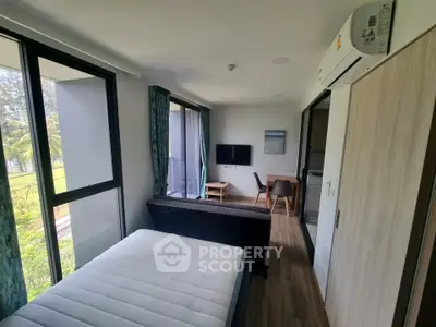 Modern bedroom with large windows and scenic view, featuring a cozy seating area and wall-mounted TV.