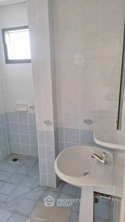 Compact bathroom with pedestal sink and tiled walls, featuring a small window for natural light.