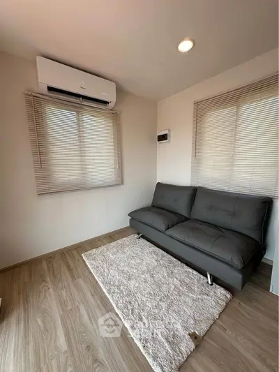 Cozy living room with modern sofa and air conditioning, featuring wooden flooring and natural light.