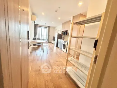 Spacious open-plan living room with modern kitchen and washing machine, featuring wooden flooring and ample natural light.