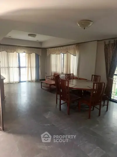 Spacious living room with elegant wooden dining set and large windows for natural light.