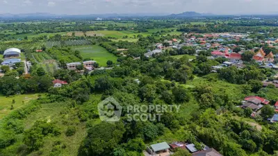 Expansive aerial view of lush green landscape with residential area and distant mountains.