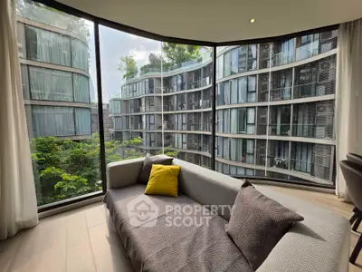 Modern living room with panoramic window view of contemporary building and lush greenery.