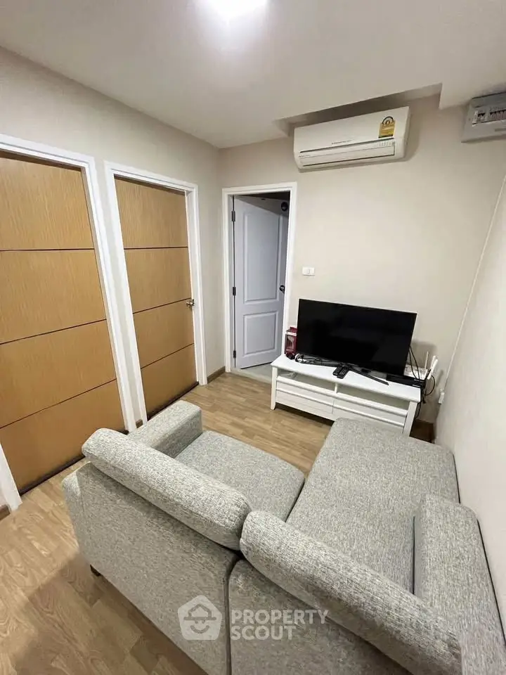 Cozy living room with modern sofa and TV, featuring wooden doors and air conditioning.