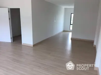 Spacious and well-lit empty living space with laminate flooring, ready for personalization, featuring large windows and a neutral color palette.