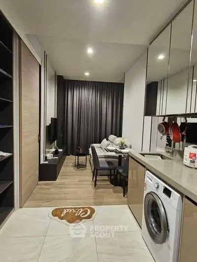 Modern open-layout living room with kitchen, featuring sleek design and washing machine, perfect for urban living.