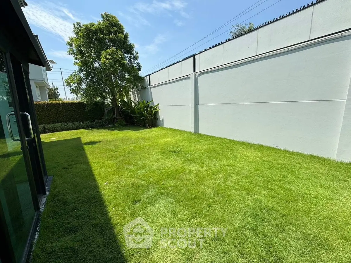 Spacious green garden with privacy wall and lush trees, perfect for outdoor activities.