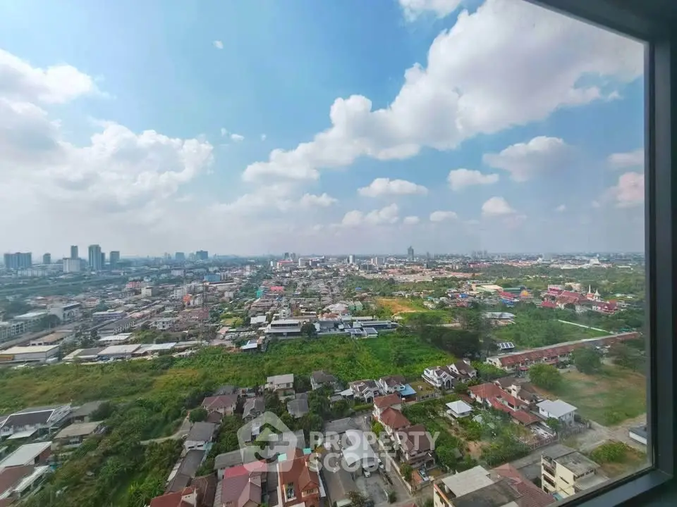 Stunning cityscape view from high-rise window showcasing urban and green landscapes under a bright blue sky.