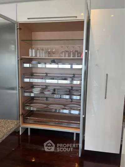Modern kitchen with sleek cabinetry and glass shelving, showcasing elegant dishware and glassware.