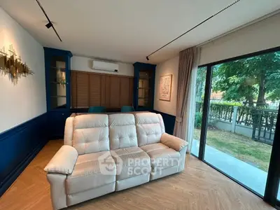 Spacious living room with elegant decor and garden view, featuring a plush white sofa and large glass doors.