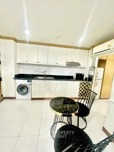 Modern kitchen with sleek cabinetry, washing machine, and elegant dining set in a bright, open space.