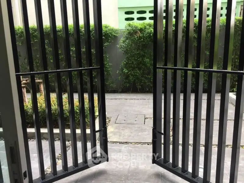 Modern garden entrance with sleek black metal gates and lush greenery