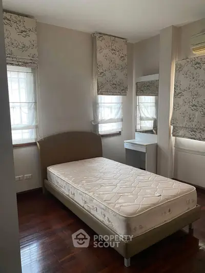 Cozy bedroom with single bed, elegant drapes, and hardwood flooring, perfect for a serene retreat.