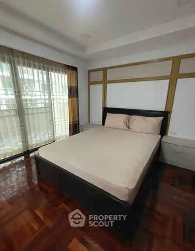 Spacious bedroom with elegant wooden flooring and large window for natural light.