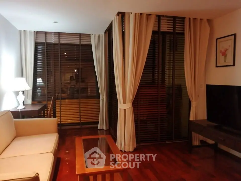 Elegant living room with wooden flooring, cozy sofa, and large windows with curtains.