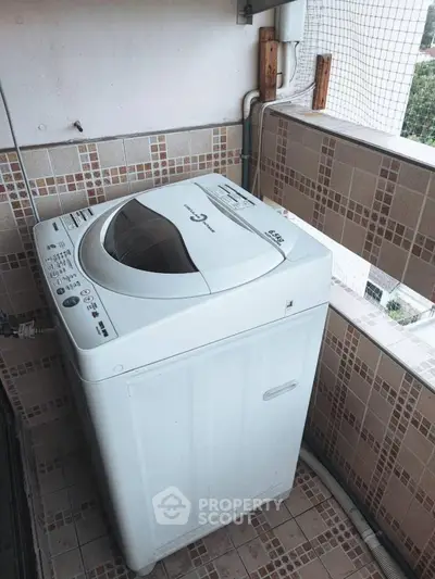 Compact washing machine on tiled balcony with partial view