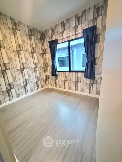 Charming empty room with stylish wallpaper and large window, perfect for customization.