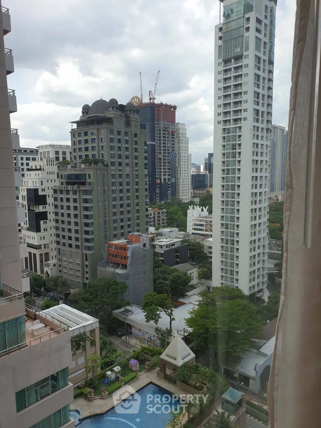 Stunning cityscape view from high-rise apartment with pool and lush greenery.