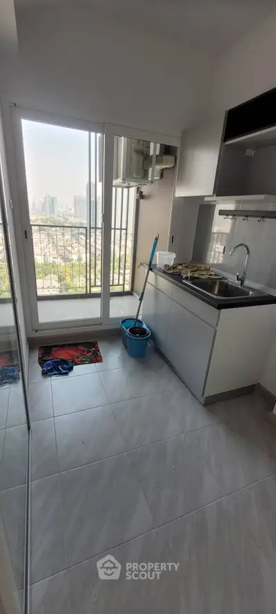 Modern kitchen with sleek cabinetry and city view from large window, featuring a mop and bucket.