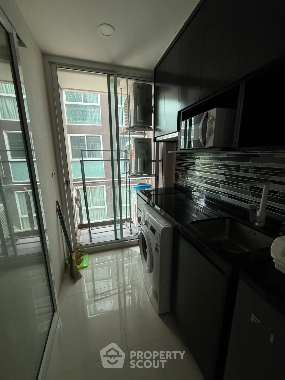 Modern kitchen with sleek cabinetry, washing machine, and balcony view in urban apartment.