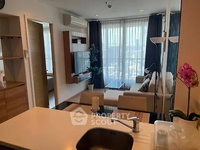 Modern living room with open kitchen, featuring stylish decor and natural light from large windows.