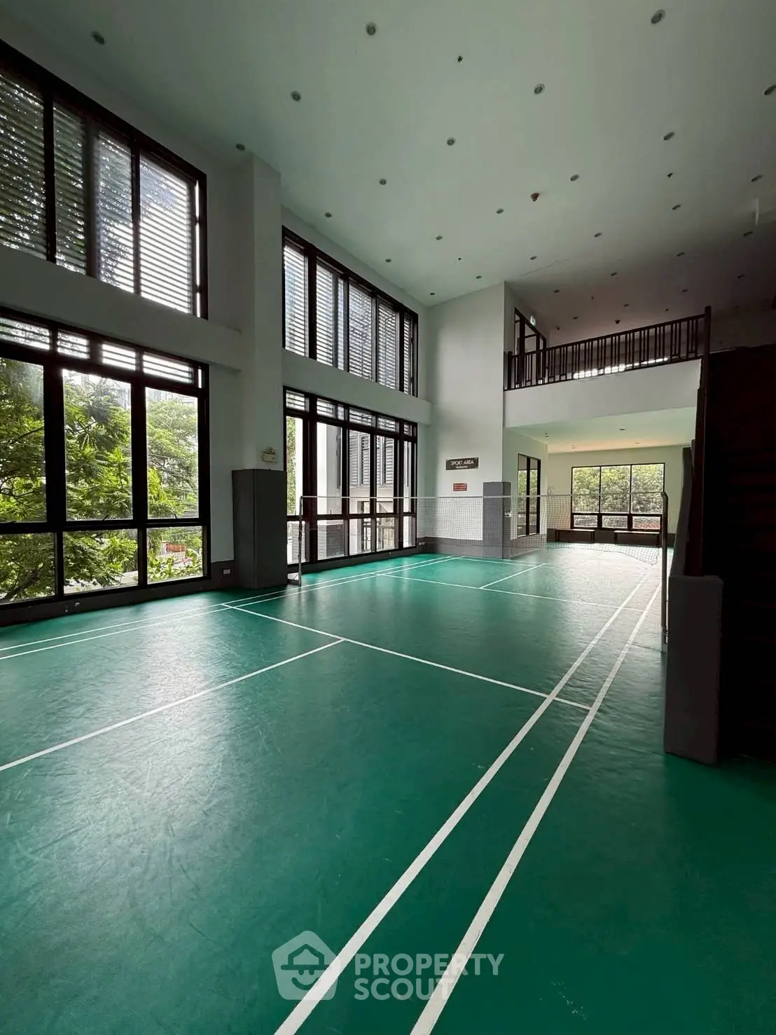 Spacious indoor sports court with high ceilings and large windows offering lush green views.
