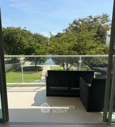 Spacious balcony with wicker furniture overlooking lush greenery and water view.