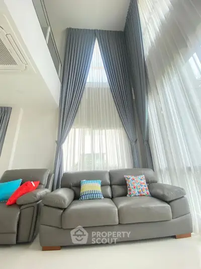 Luxurious high-ceiling living room with elegant curtains and modern leather sofa.