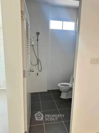 Modern bathroom with sleek tiles and natural light, featuring a shower and toilet.
