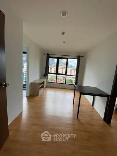 Spacious living room with large window offering city views and wooden flooring.