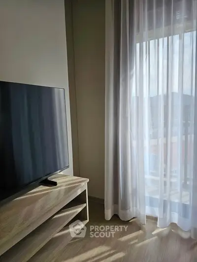Modern living room with TV and sheer curtains letting in natural light.