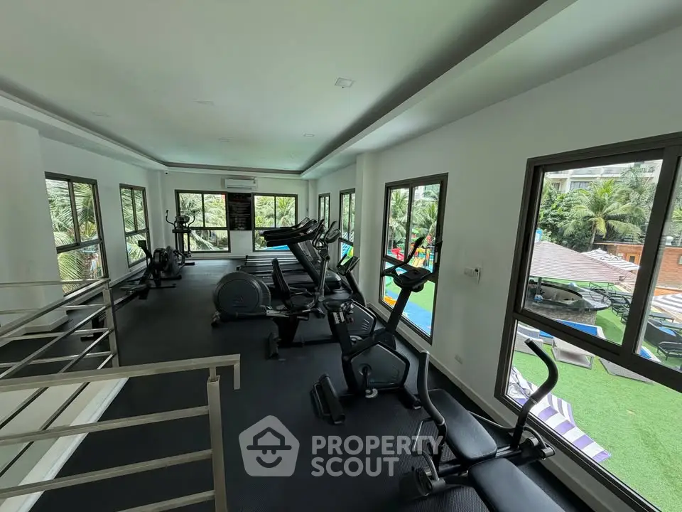 Modern gym with exercise equipment and pool view in luxury residential complex.