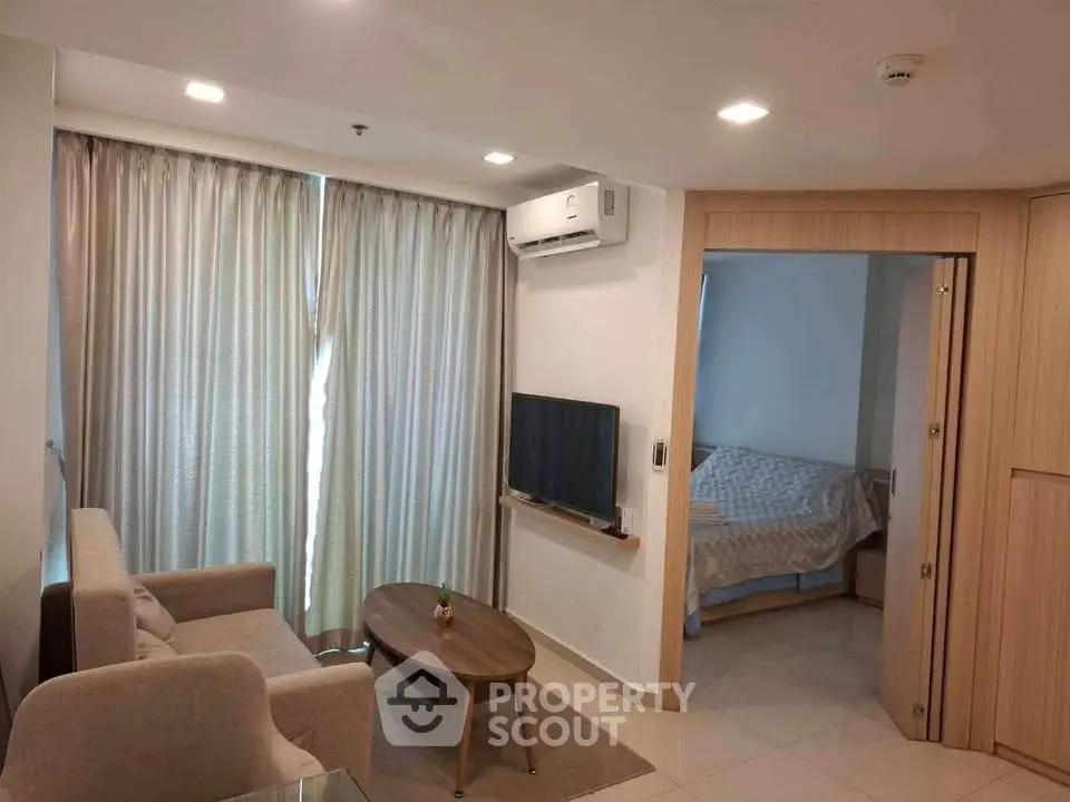 Modern living room with cozy sofa, wall-mounted TV, and adjacent bedroom in open layout apartment.