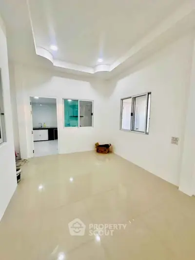 Spacious unfurnished room with tiled flooring and recessed lighting, adjacent to a modern kitchen.