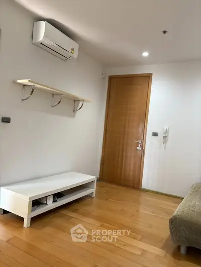 Modern living room with wooden flooring, air conditioning, and minimalist furniture.