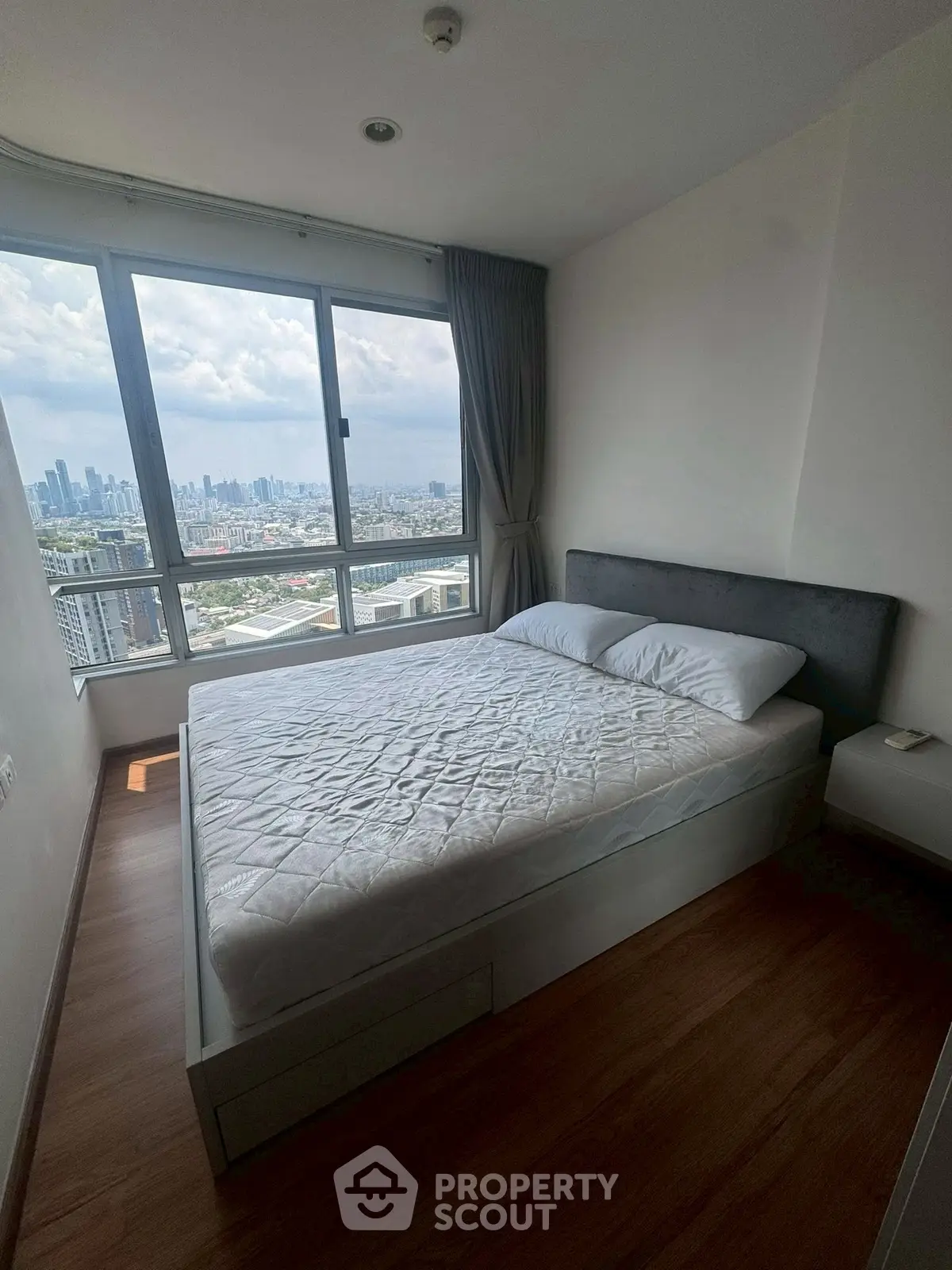 Modern bedroom with stunning city view and large window in high-rise apartment.